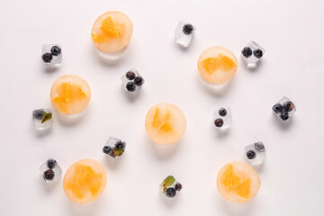 Pieces of fresh orange and blueberry frozen in ice on light background