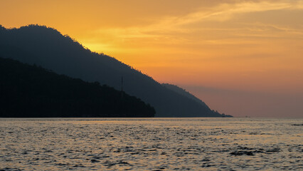 Silhouetted peninsula of tropical islands against a golden orange sky and placid ocean view in Raja...