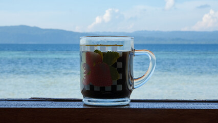 A glass cup of coffee with beautiful blue ocean water in the background in tropical destination of Raja Ampat, West Papua, Indonesia