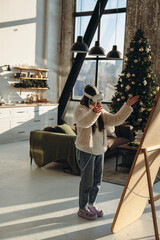 With the Christmas mood around, a young woman in light clothing and a virtual reality headset stands before the mirror.