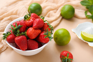 Bowl with ripe strawberry and lime on beige background, closeup