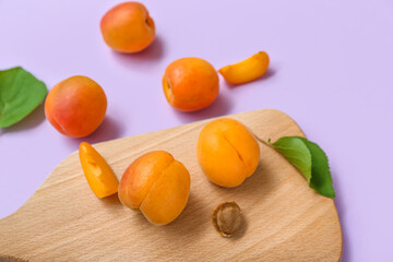 Board with fresh apricots and leaves on lilac background