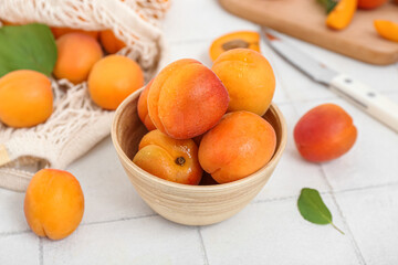 Bowl and string bag with fresh apricots on white tile table