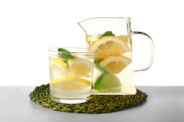 Glass and jug of infused water with lemon on white background