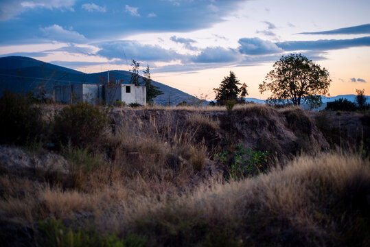 Paisaje. Chosa de concreto en cerro con monta&ntilde;as y hierba alta seca al rededor, con monta&ntilde;as al fondo a la hora del atardecer.