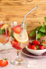 Glasses of fresh lemonade with strawberry and lemon on pink tile table