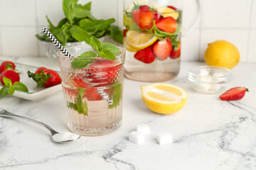 Glass and jug of fresh lemonade with strawberry on white table