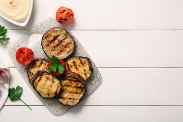 Delicious grilled eggplants, sauce and tomatoes on white wooden background
