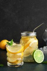 Glass and mason jar of infused water with lemon on black background