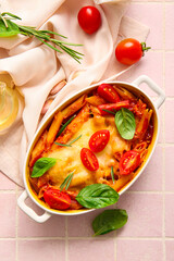 Baking dish of pasta with tomato sauce and cheese on pink tile background