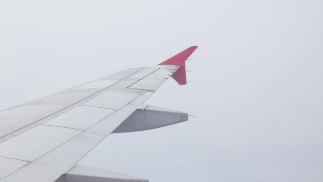 view through plane window from inside airplane cabin while climbing flying over the sky with airplane wing winglet and fluffy cloud outside