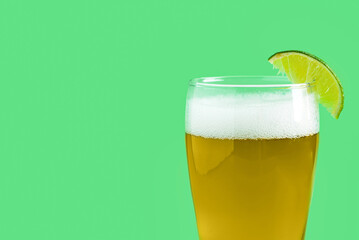 Glass of cold beer with lime on green background