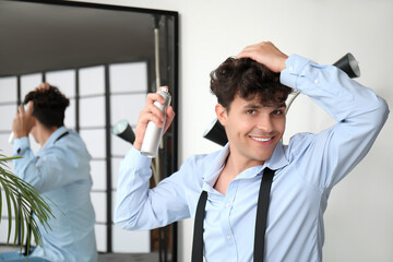 Fototapeta premium Handsome young man applying hair spray on his curly hair near mirror
