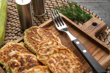 Wooden board of tasty zucchini fritters on table
