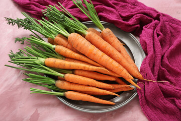 Plate with fresh carrots on pink background