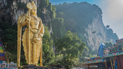 The famous Batu caves. In front of the entrance, a huge golden statue of the god Murugan against...