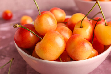 Bowl with sweet yellow cherries on purple background