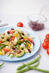 Plate of tasty pasta salad with tomatoes and beans on white background