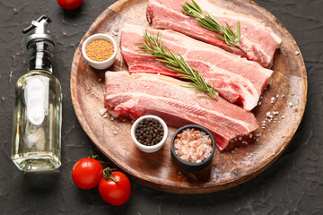 Wooden plate with raw pork ribs, tomatoes, spices and oil on dark background, closeup