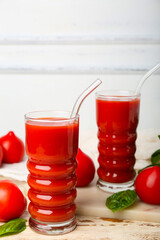 Glasses of tasty tomato juice on white wooden background