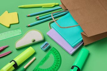 Composition with paper bag and different stationery on green background, closeup