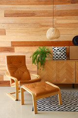 Brown armchair with footstool and sideboard near wooden wall