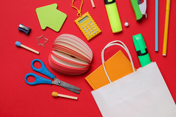 Shopping bag with different school stationery on red background