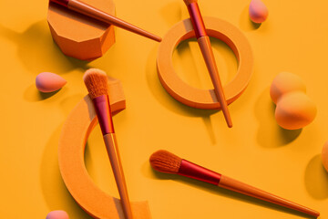 Decorative podiums with makeup brushes and sponges on yellow background
