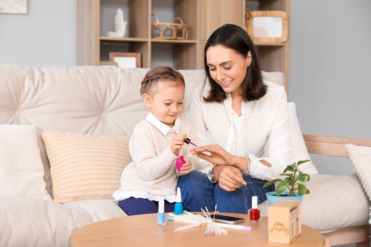 Cute little daughter doing nails of her beautiful mother at home