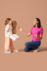 Cute little daughter greeting her beautiful mother with gift box and bouquet of roses on brown background. Happy  Mother's Day
