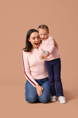 Beautiful mother and her cute little daughter with mobile phone on brown background