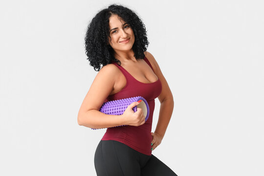 Sporty adult woman with body roller on grey background