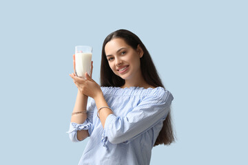 Young woman with glass of tasty milk on blue background