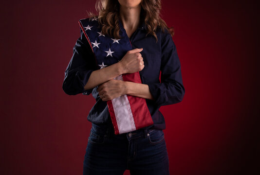 A woman holding an American flag across her chest - Powered by Adobe