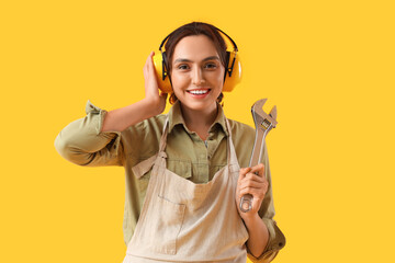 Female worker in hearing protectors with wrench on yellow background