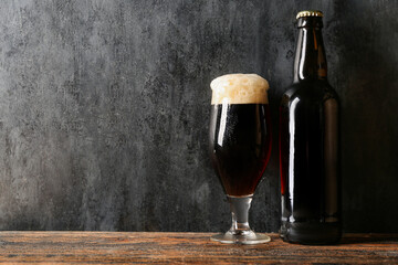 Glass and bottle of cold dark beer on wooden table against black grunge background