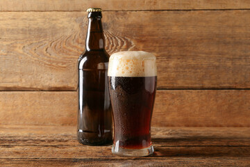 Glass and bottle of cold dark beer on table against wooden background