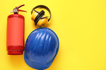 Fire extinguisher, hearing protectors and helmet on yellow background