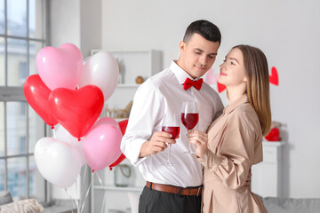 Beautiful young couple with heart-shaped balloons and glasses of wine celebrating Valentine's Day at home