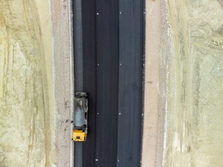 yellow truck pouring bitumen over a new road. Aerial drone shot. Road construction in progress on slope nature canyon. Infrastructure development and logistics.