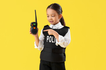 Cute little police officer pointing at radio transmitter on yellow background. Opposite Day...