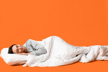 Pretty young woman with blanket sleeping on orange background