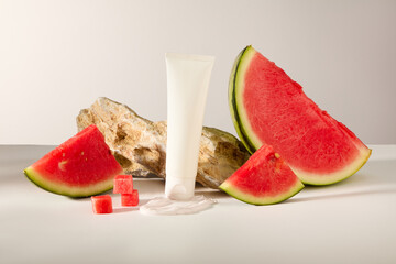 Unlabeled white tube decorated with watermelon and a white cream smear. A block of stone displayed behind. Empty label for branding mockup of Watermelon extract