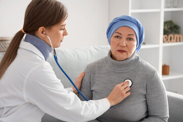 Doctor listening lungs of mature woman after chemotherapy with stethoscope at home. Stomach cancer...