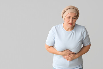 Mature woman after chemotherapy suffering from pain on light background. Stomach cancer concept