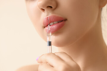 Young woman with lip injection on beige background, closeup