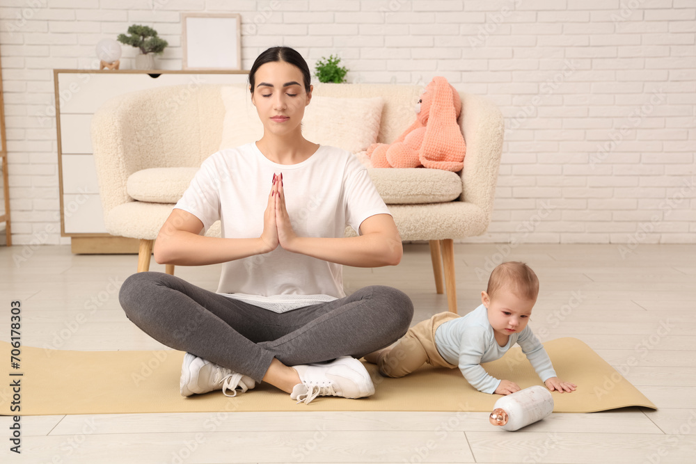 Poster Beautiful young sporty woman with her little baby meditating at home