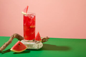 A glass juice of watermelon displayed on stone podium with dried twig and watermelon slices on a pink background. Copy space. True to its name, watermelon is made of 90% water