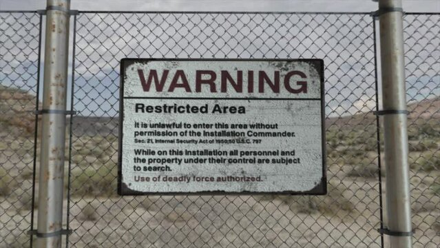 High quality 3D CGI render with a smooth dollying-in shot of a chainlink fence at a high security installation in a desert scene, with a Warning Restricted Area sign
