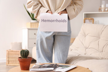 Mature woman with word HEMORRHOIDS at home, back view - obrazy, fototapety, plakaty